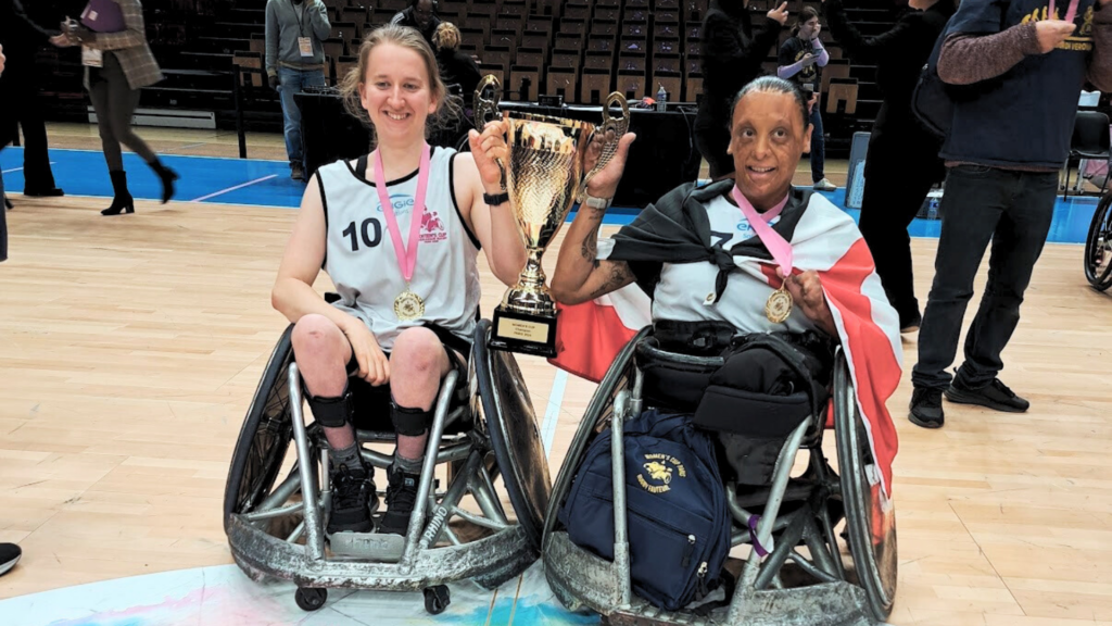 Two women in sports wheelchairs raise a trophy in celebration. On the left is Wheelcahir rugby player Jacinta Richardson and on the right is Wheelchair rugby player Maia Marshall-Amai.