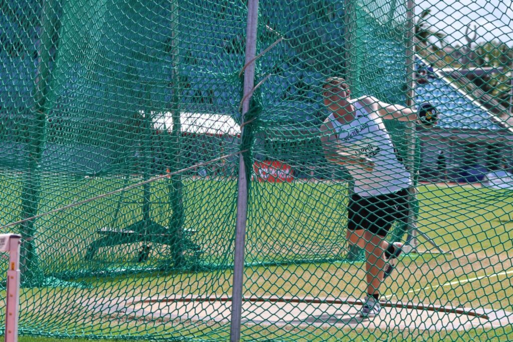 Para athlete Zack Lappin throws a discus behind a green net.