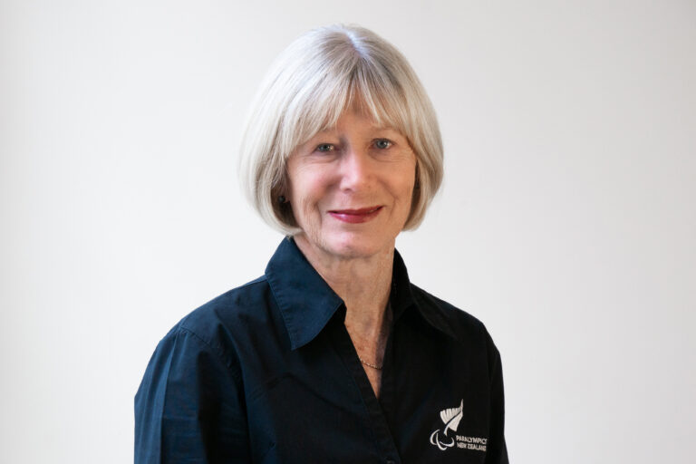 Professional portrait of Marguerite Christophers wearing a Paralympics New Zealand uniform. She has fair skin with mid length grey hair cut above the shoulder.