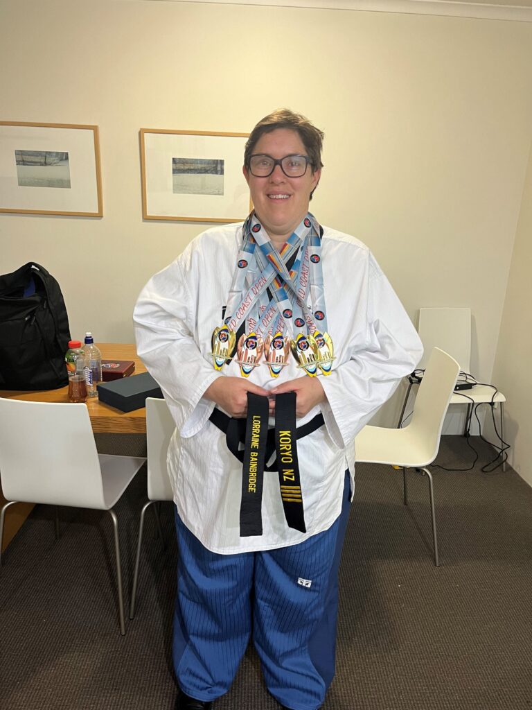 A Para taekwondo athlete stands in a white uniform with a black belt and numerous medals around their neck. 