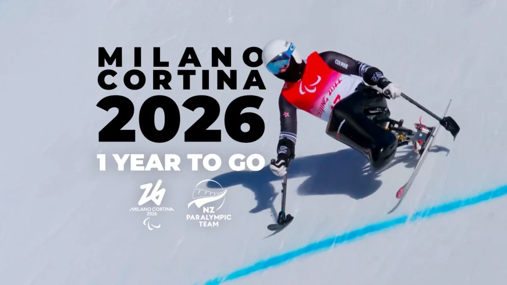 Corey Peters skis down a steep ski slope as text appears to his left reading "Milano Cortina 2026: 1 Year to Go." Logos sit beneath for Milano Cortina 2026 and the NZ Paralympic Team.