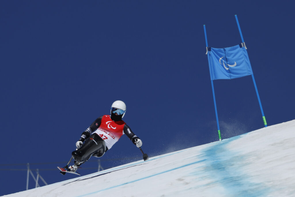 Para alpine ski racer Corey Peters soars around a bend with a deep blue ski behind him.