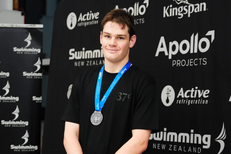 James Haydon smiles while receiving a silver medal on a swimming competition podium.