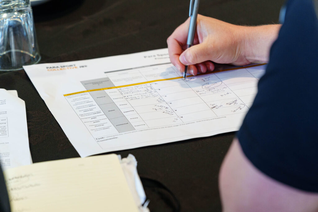 A participant writes into a worksheet titled "Para Sport Pathway Roles" on a table at the Para Sport Collective Hui hosted by Paralympics New Zealand on 25 August 2025.
