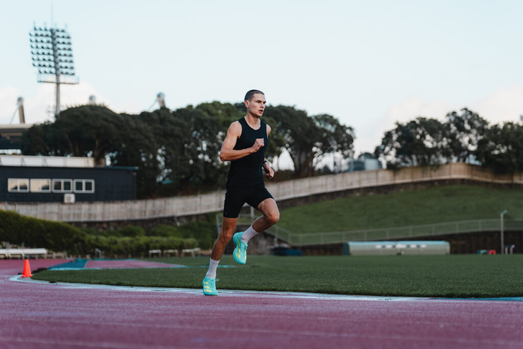 Michael Whittaker runs on an athletics track under a cool evening light.