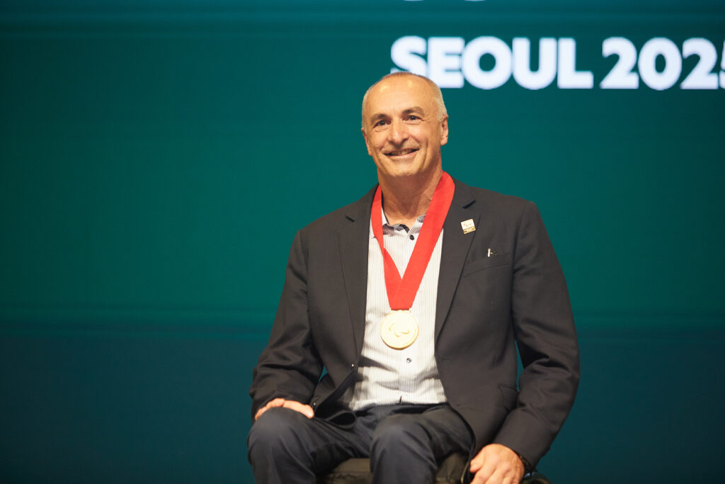 Duane Kale smiles on stage as he wears his medal of the Paralympic Order.