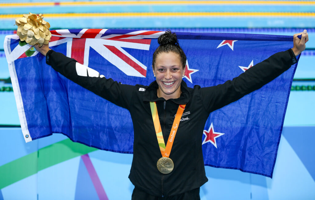 Sophie Pascoe celebrates poolside at the Rio 2016 Paralympic Games with the NZ flag in her arms and a gold medal around her neck.