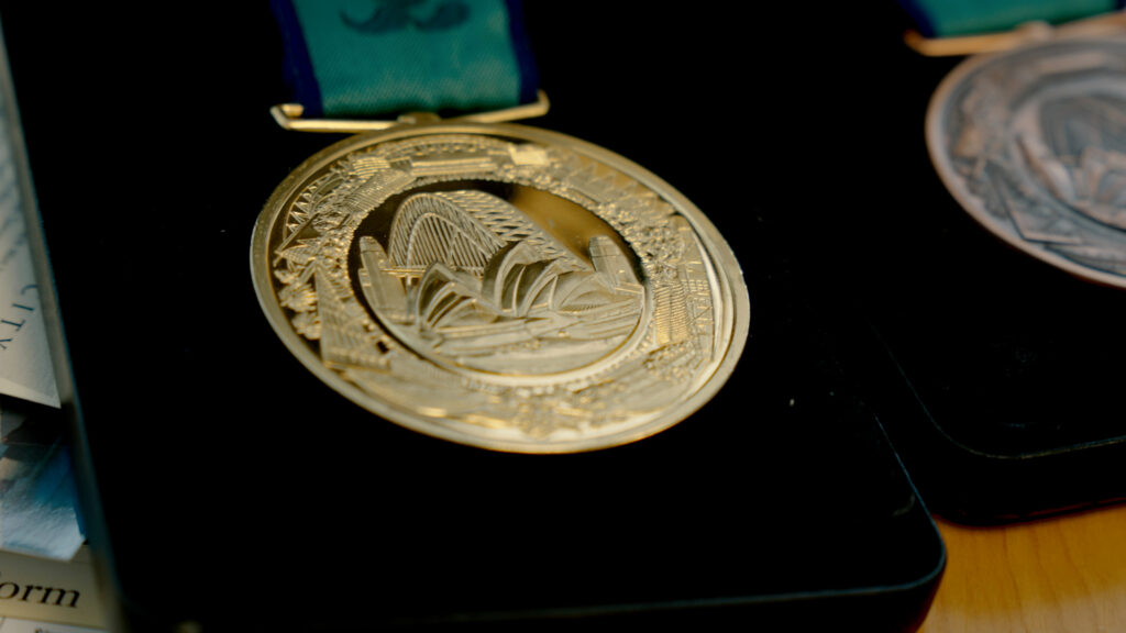A close up photo of the gold medal from the Sydney 2000 Paralympic Games. It shows the iconic Opera house and harbour bridge embossed on the face.