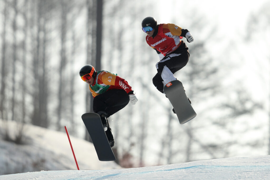 Two Para snowboarders jump over a berm in the Para snowboard cross at Pyeongchang 2018.