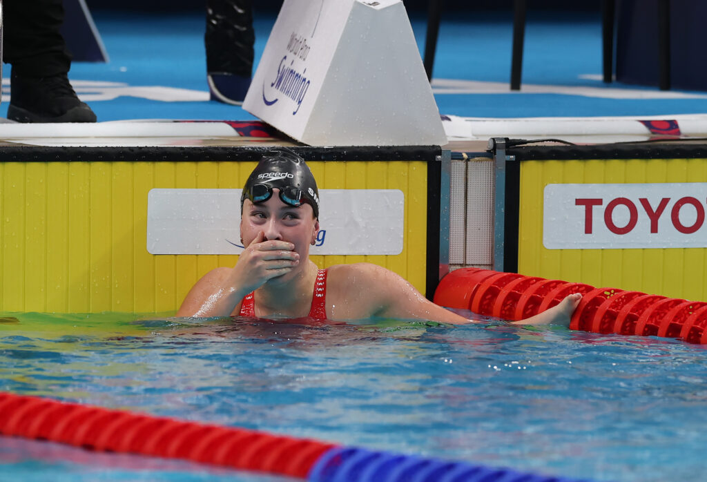 Gaby covers her mouth in shock as she looks at the scoreboard from the pool.