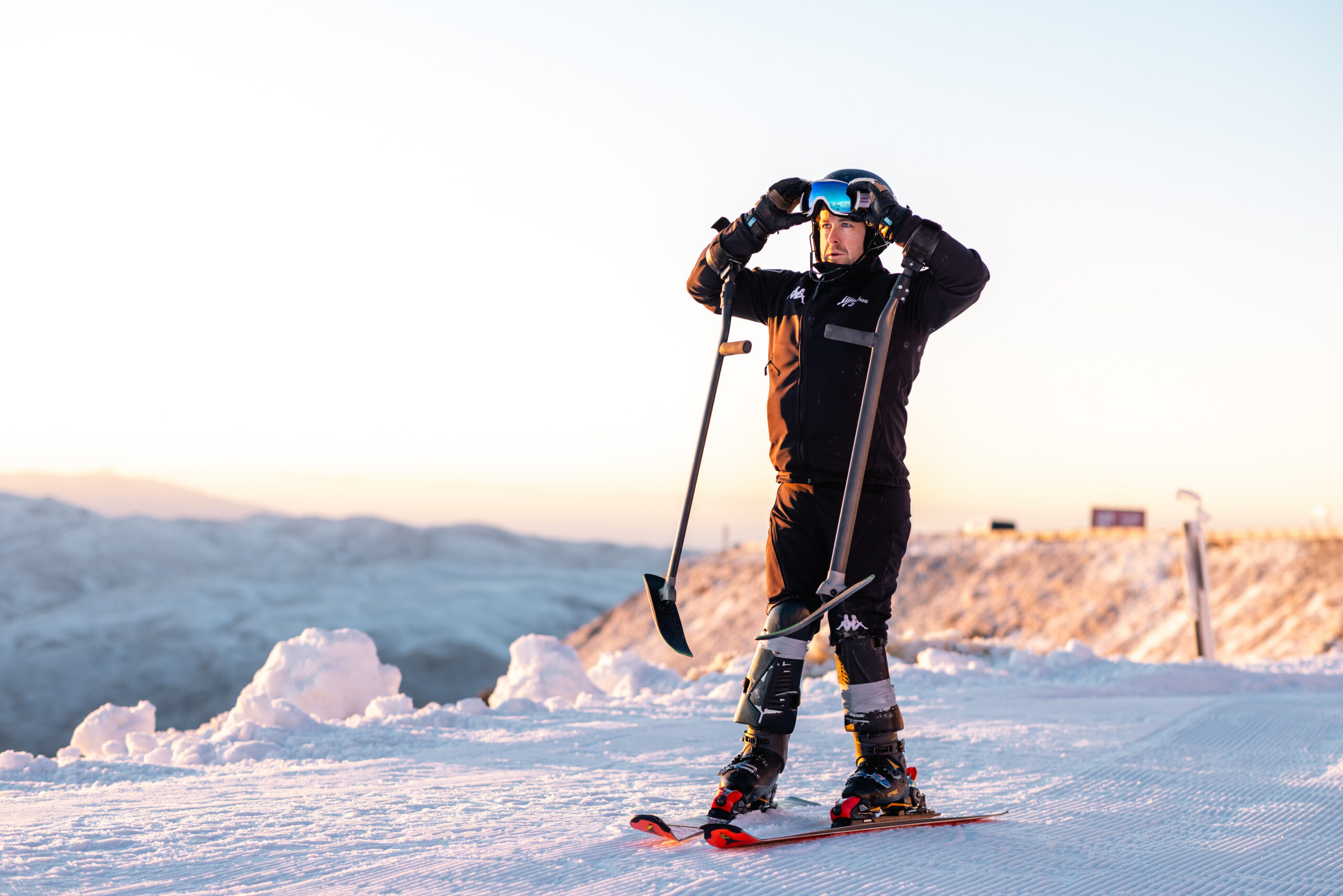 Adam Hall pulls his goggles down atop a mountain at sunrise.