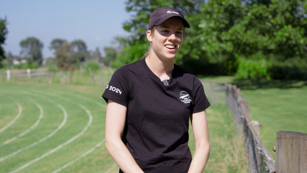 Danielle Aitchison stands on a field with an athletics track painted on the grass.