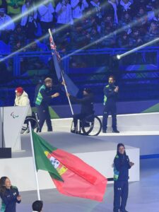 A man in a wheelchair accepting a New Zealand flag on a pole.