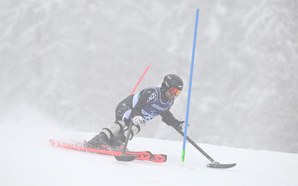 Adam Hall competes in snowy conditions and poor visibility by a blue gate at the Men's Slalom Standing at Milano Cortina 2026.