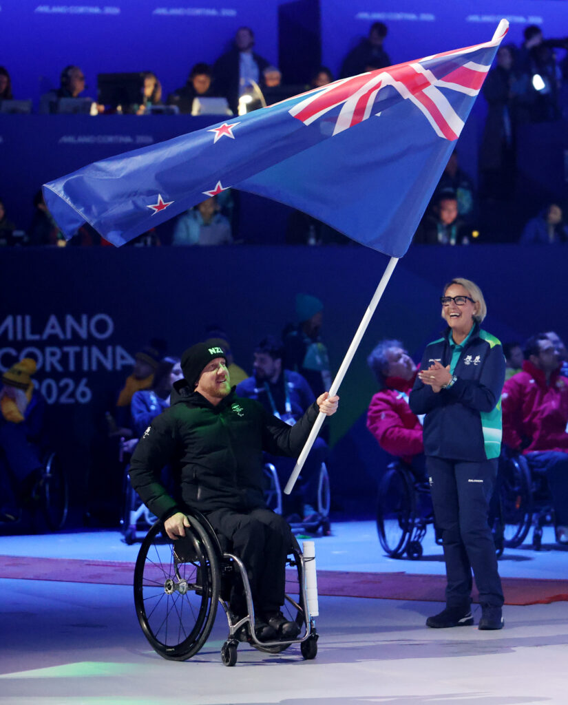 Paralympian Corey Peters pictured sat in a wheelchair as NZ Paralympic Team Closing Ceremony Flagbearer. He is holding the New Zealand flag.