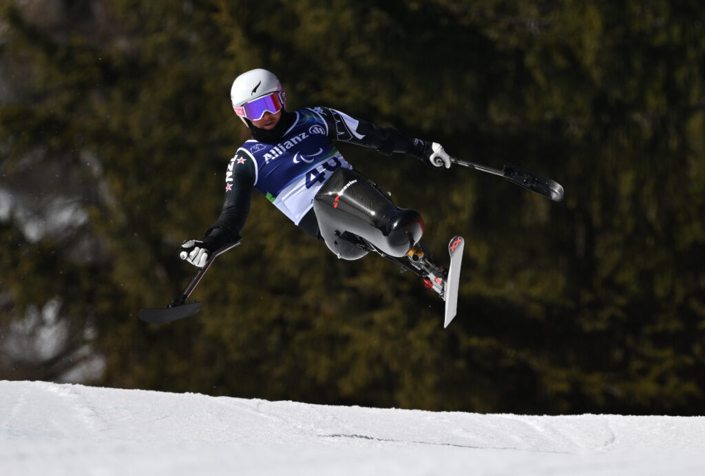 Corey Peters skis in the Men's Downhill Sitting at Milano Cortina 2026. His sit-ski lifts off the snow in a bumpy region of the course. 