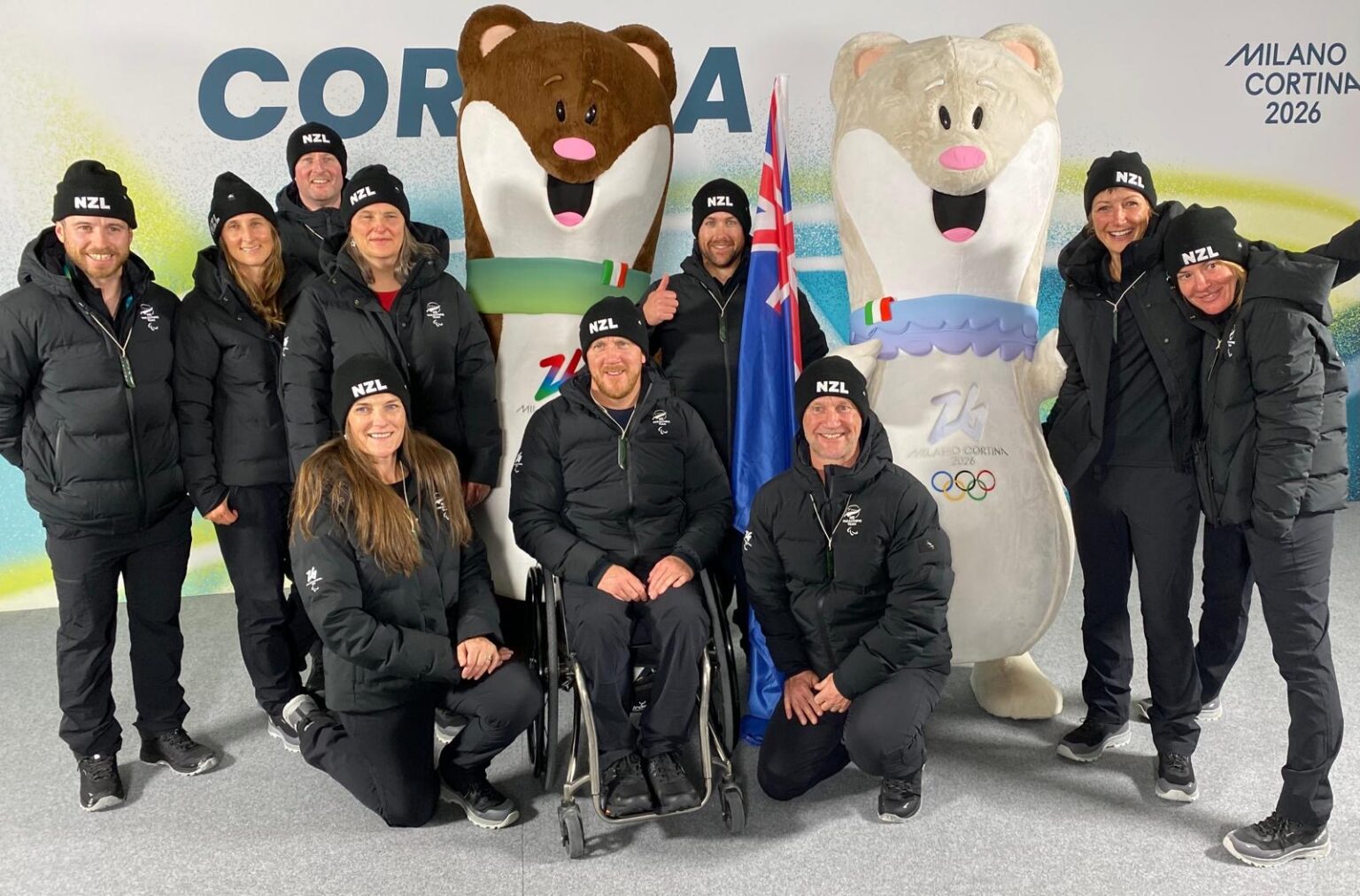 Image of the NZ Paralympic Team with Adam Hall (centre) as the flag bearer pictured with two mascots.