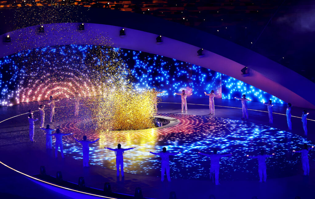 The Opening Ceremony of the Milano Cortina 2026 Paralympic Winter Games shows floods of blue light and a burst of orange light in the centre of the arena. 