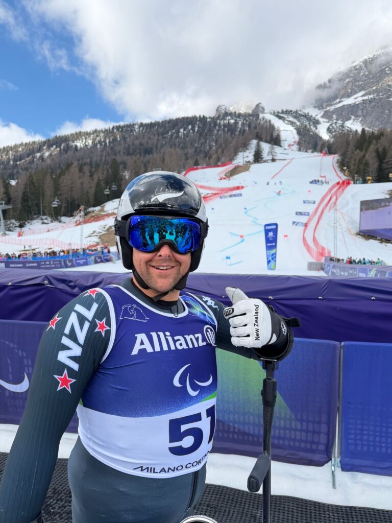 Man on skis at bottom of ski run smiling with thumbs up
