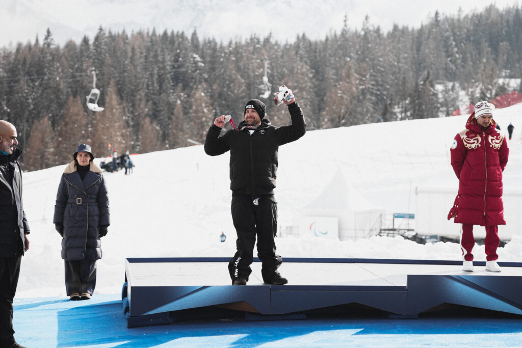 Adam Hall raises his silver medal on the podium at the Milano Cortina 2026 Paralympic Winter Games.