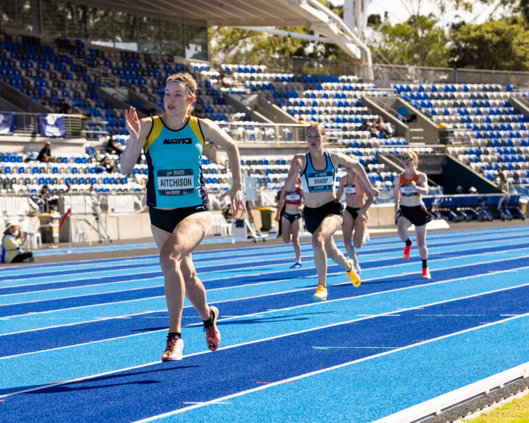 Danielle Aitchison runs on an athletics track and leads the field.