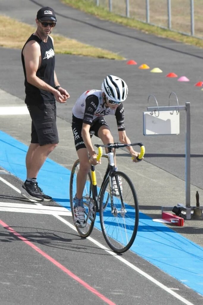 A young cyclists sets off from a starting position on track. A man, Felix, observes from aside. 