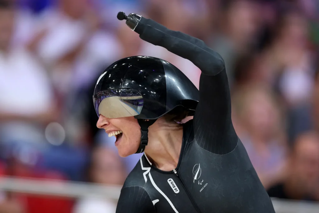 Nicole Murray raises her prosthetic arm in the air at the end of a race at Paris 2024. Sher wears a cycling helmet.