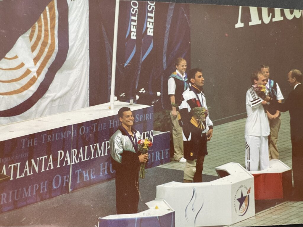 Aaron Bidois holds a bouquet of flowers and wears a silver medal on the podium at Atlanta 1996.
